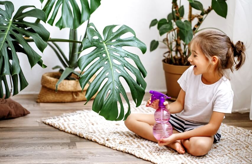 little girl spraying water on plant